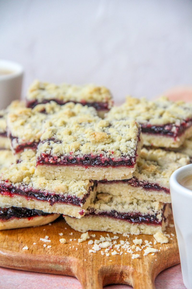 Estonian Jam Bars (Klassikaline Purukook) sit stacked on each other on a wooden board on a pink surface.