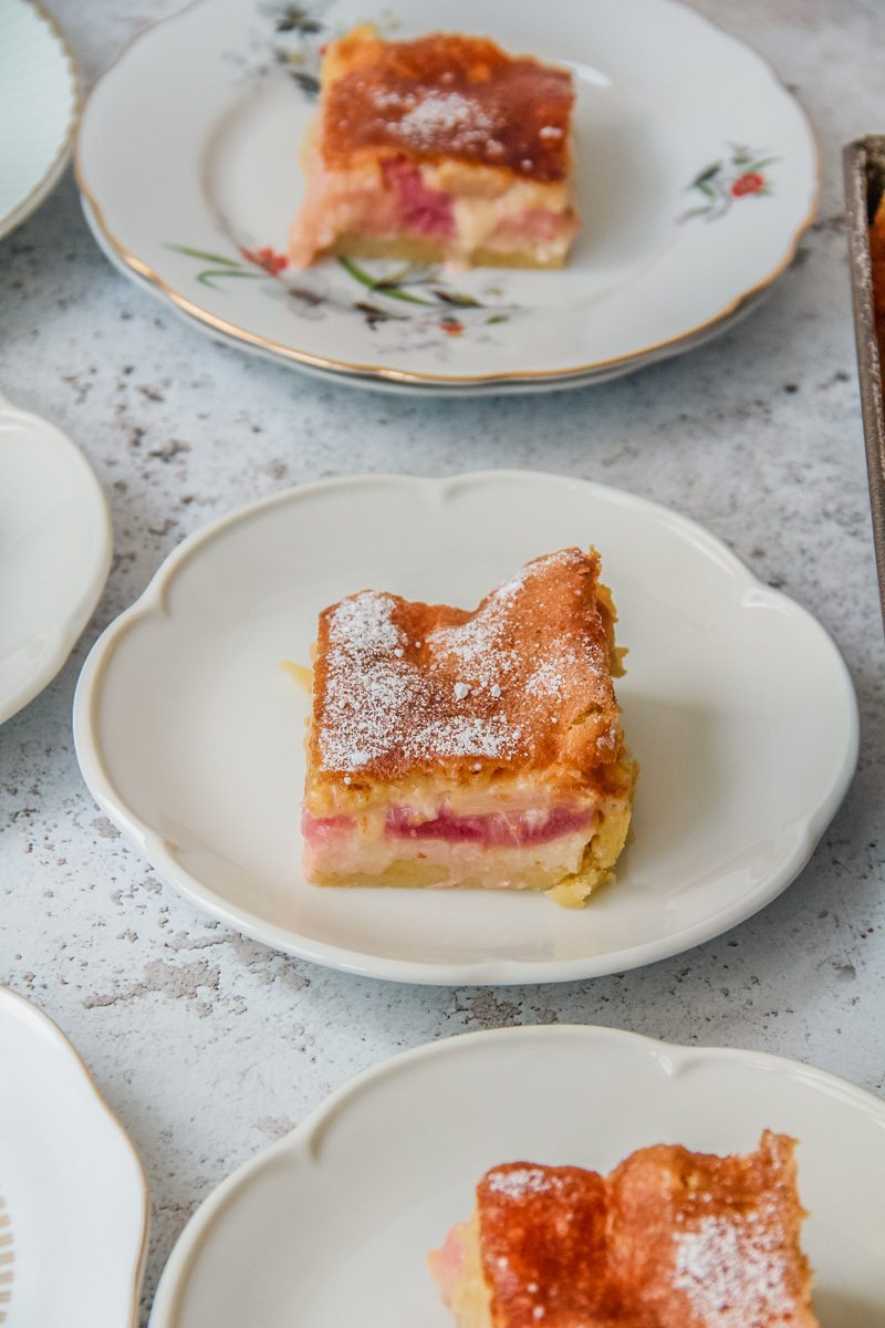 Slices of Estonian rhubarb cake sit on fluted ceramic plates on a light gray surface.