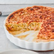 A Flamiche tart with it's leek and bacon interior visible sits in a white ceramic tart dish on a gray surface.