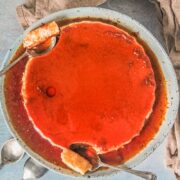 Spoonfuls of flan rest beside a large flan sitting on a rimmed blue ceramic plate above a gray surface.