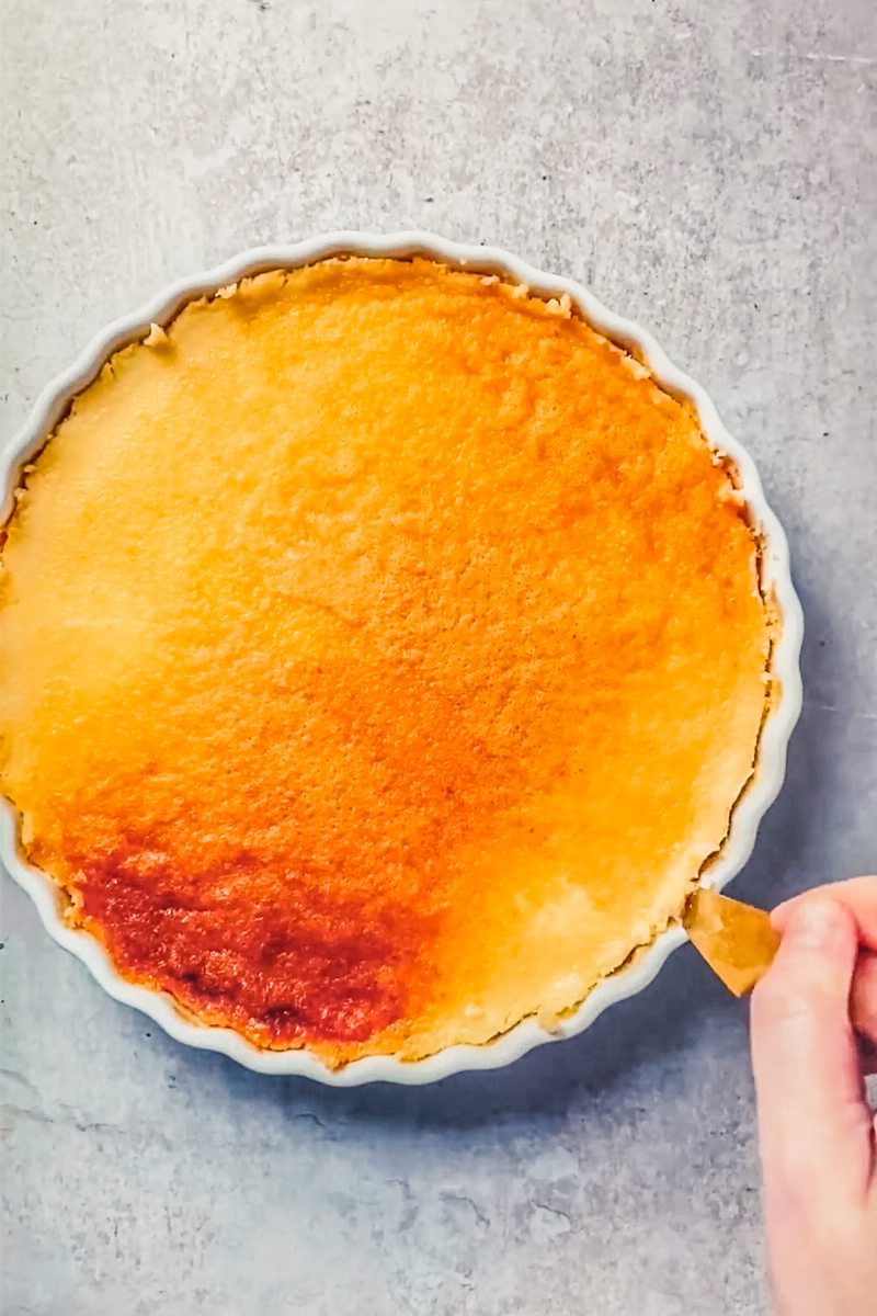 The edges of flan are loosened in a white ceramic baking dish on a gray surface.