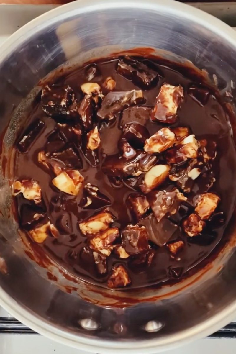 Cubes of chocolate and butter melt in a stainless steel saucepan on a cooker.