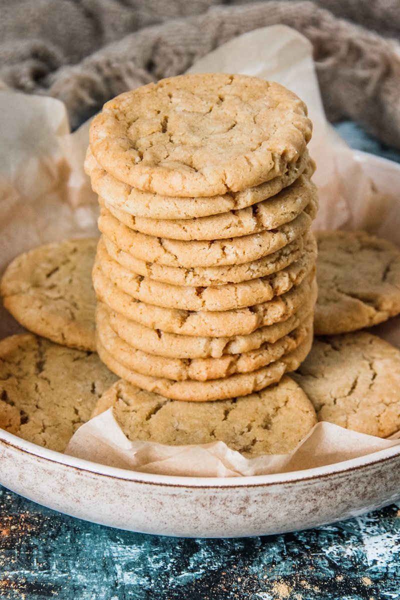 Cornish Fairing biscuits sit stacked on a rimmed ceramic plate lined with parchment paper above a green and white surface.