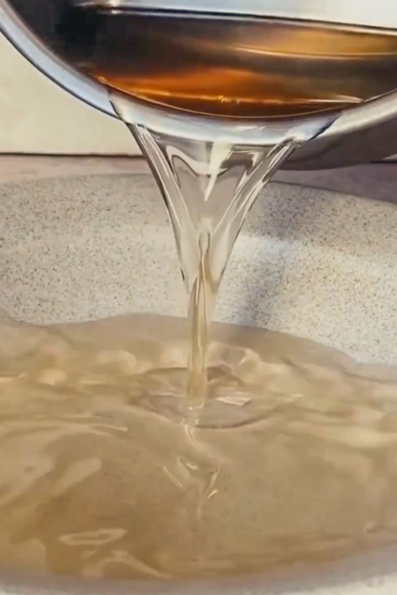 Syrup is poured from a stainless steel saucepan into a gray ceramic low bowl.