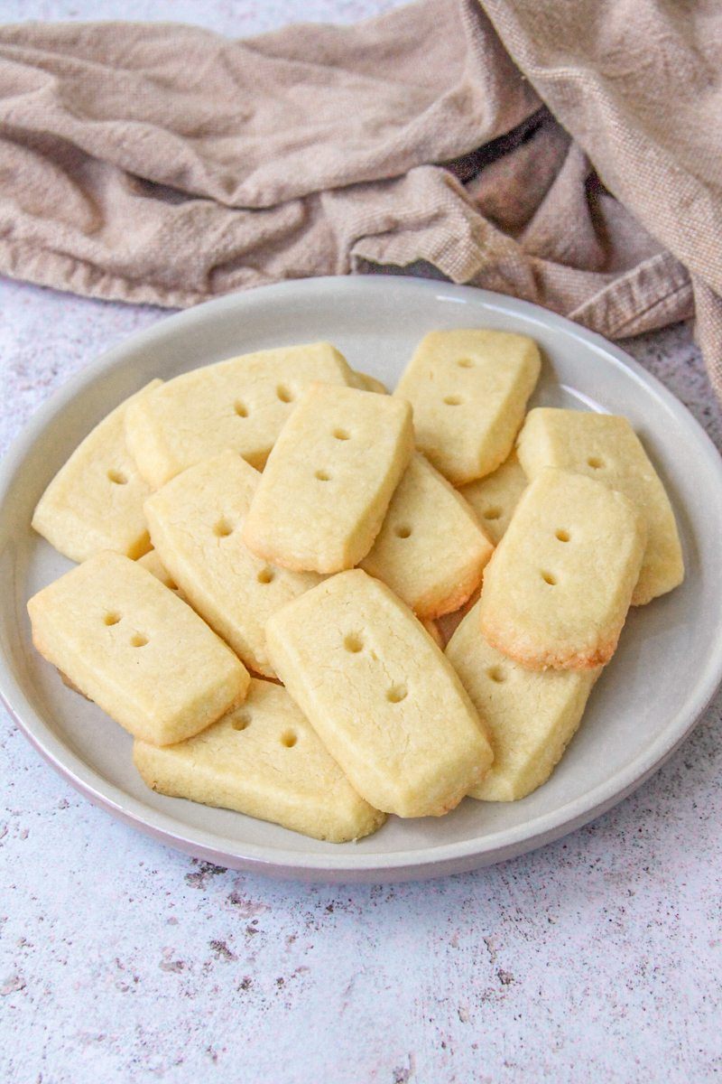 Shortbread sit on a deep plate on a gray surface with a brown cloth behind.