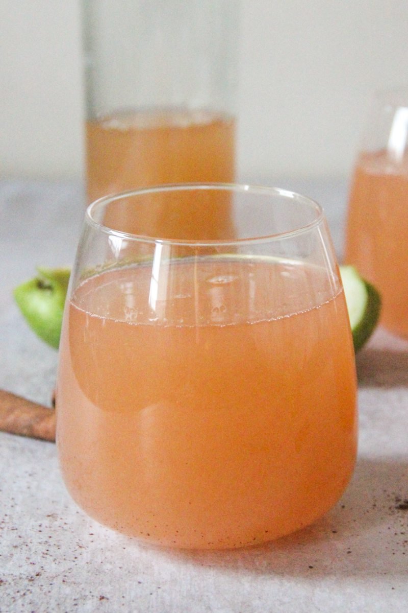 A low ball glass sits on a gray surface with golden homemade apple cider inside.