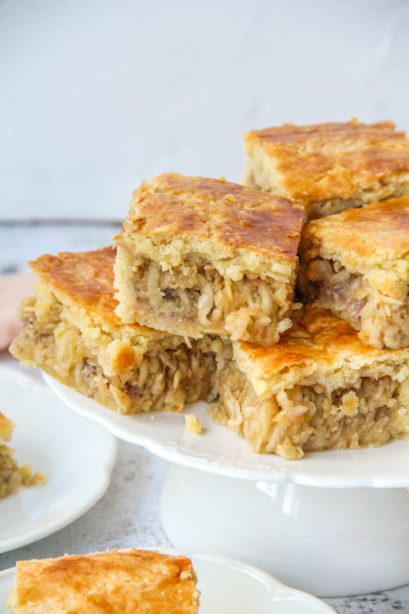 A close up of Hungarian Apple Pie sit on a serving plate above individual servings on a light gray surface.