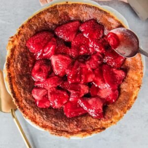 Homemade strawberry jam is spooned on top of a Hungarian Rice Pudding Cake served up with a coral cloth on a light gray surface.