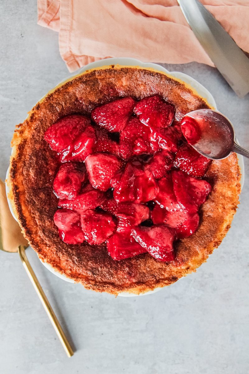 Homemade strawberry jam is spooned on top of a Hungarian Rice Pudding Cake served up with a coral cloth on a light gray surface.