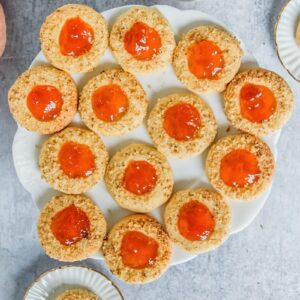 A plate of Hungarian Thumbprint cookies sit on a light gray surface with a cup of tea beside.