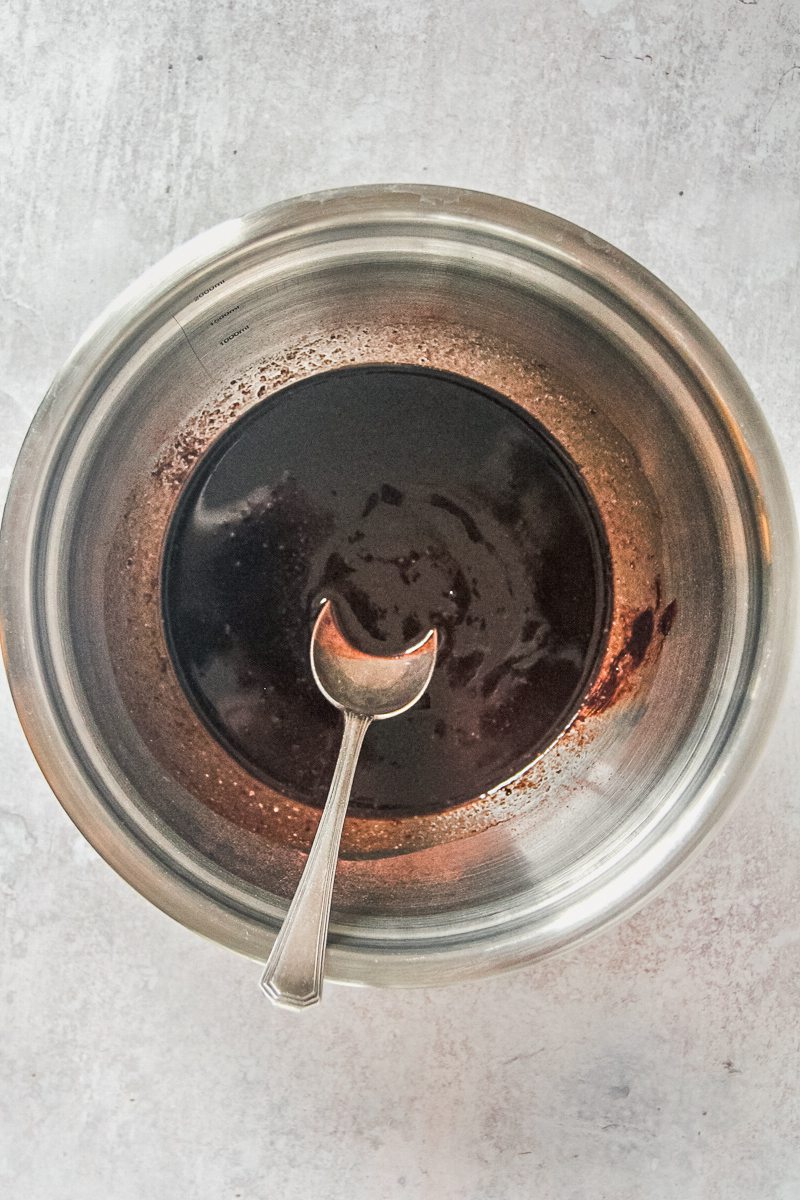 A cocoa and melted butter mixture sits in a stainless steel bowl on a gray surface.