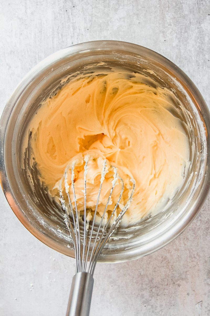 A whipped custard buttercream sits in a stainless steel bowl on a gray surface.