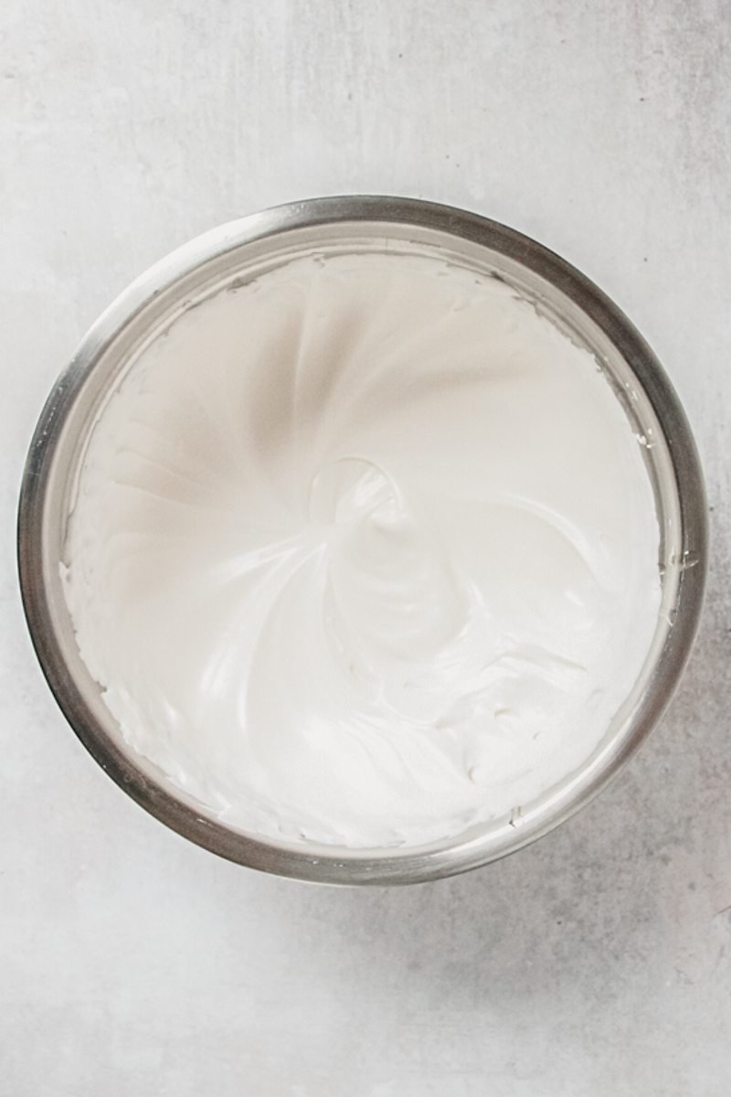 Whipped marshmallow sits in a stainless steel saucepan on a gray surface.