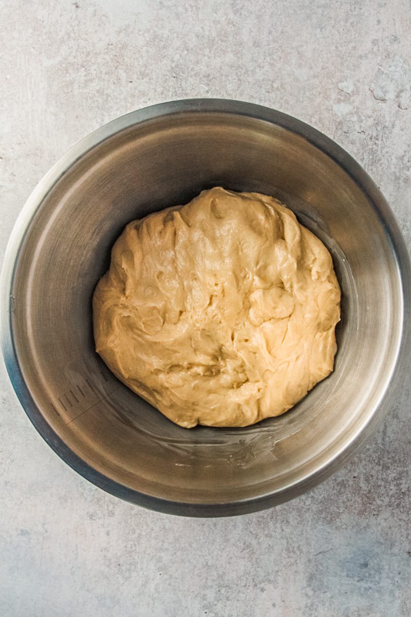 A smooth dough sits in a stainless steel bowl on a gray surface.