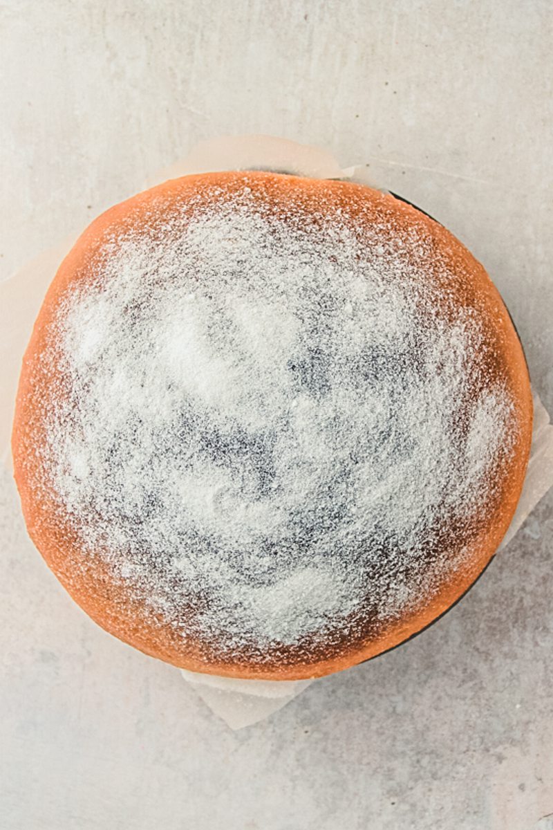 A Sufganiyot or Donut cake sits on a gray surface with a sprinkle of sugar on topping.