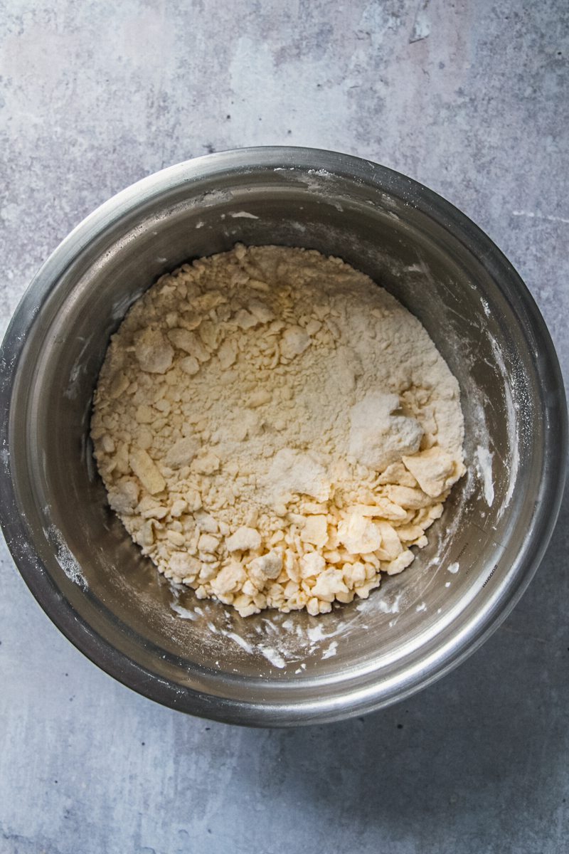 A crumble mixture sits in a stainless steel bowl on a gray surface.