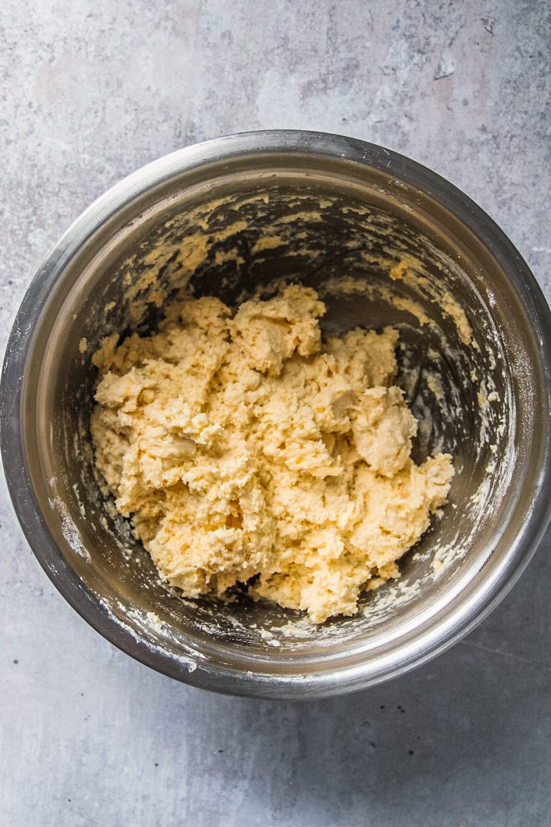 A cobbler dough sits in a stainless steel bowl on a gray surface.