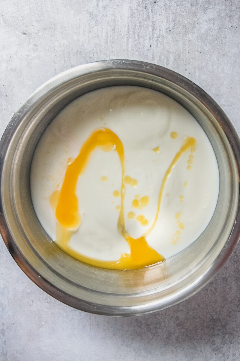 Melted butter sits on top of buttermilk in a stainless steel bowl on a gray surface.