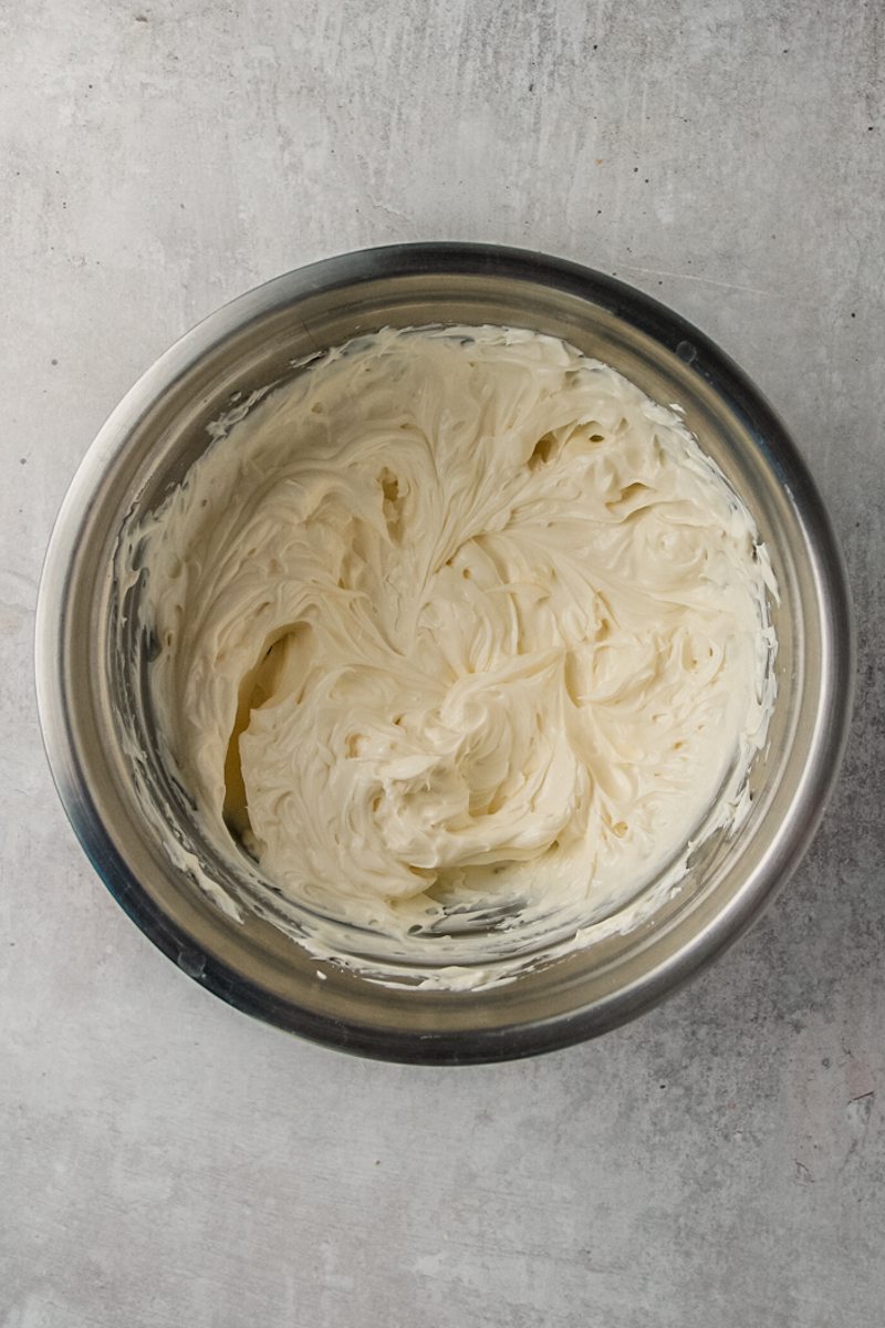 Whipped cream cheese sits in a stainless steel bowl on a gray surface.