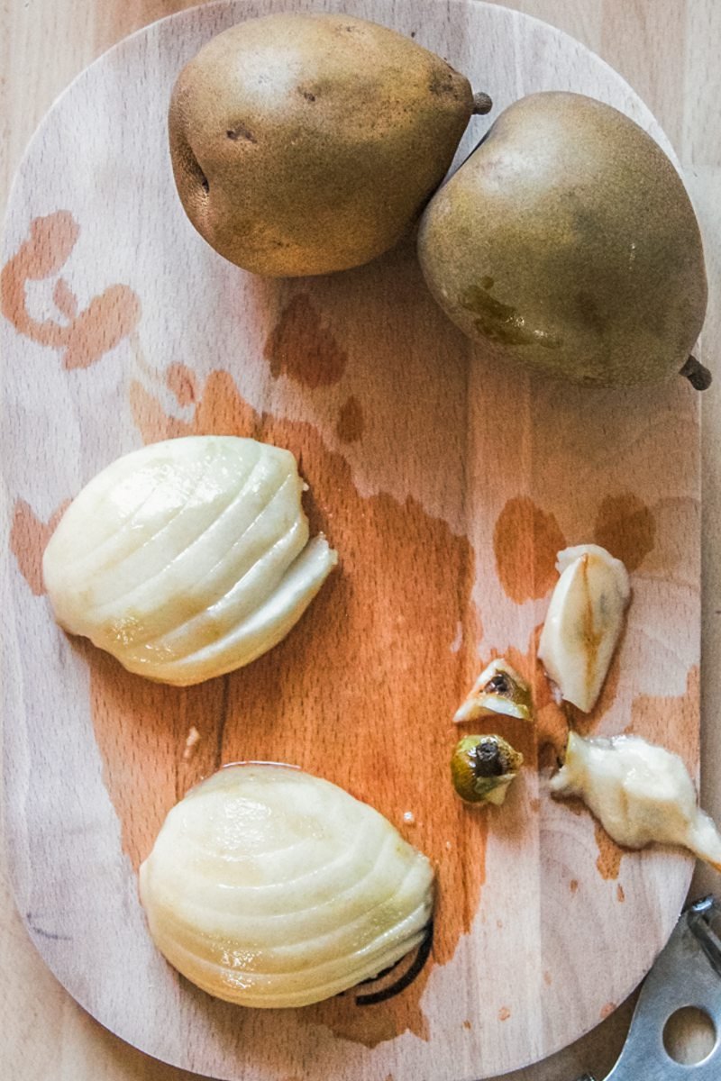 Peeled, cored and sliced pears sit on a wooden board beside whole pears.