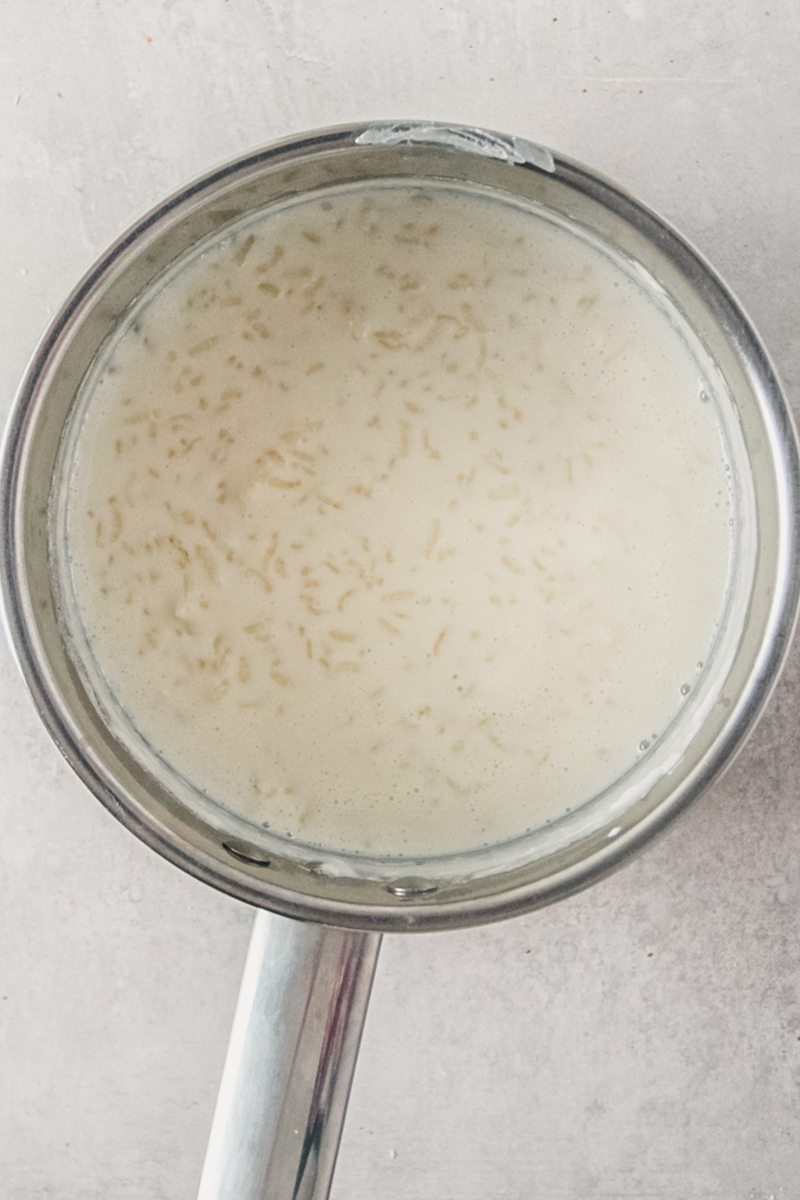 Rice pudding sits in a stainless steel saucepan on a gray surface.