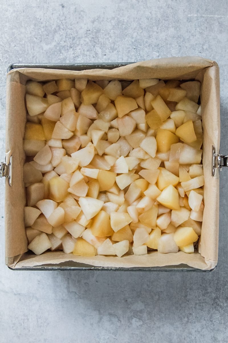 Cooked cubed apples sit in a square lined metal tin on a gray surface.