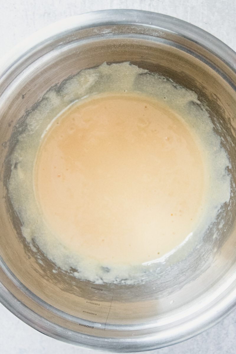 Whisked egg yolks and sugar sit in a stainless steel bowl on a gray surface.