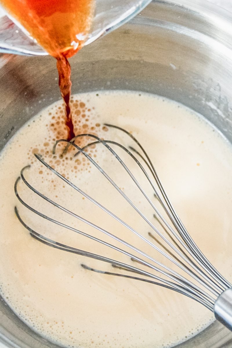 Coffee is poured into a custard in a stainless steel bowl with a whisk.