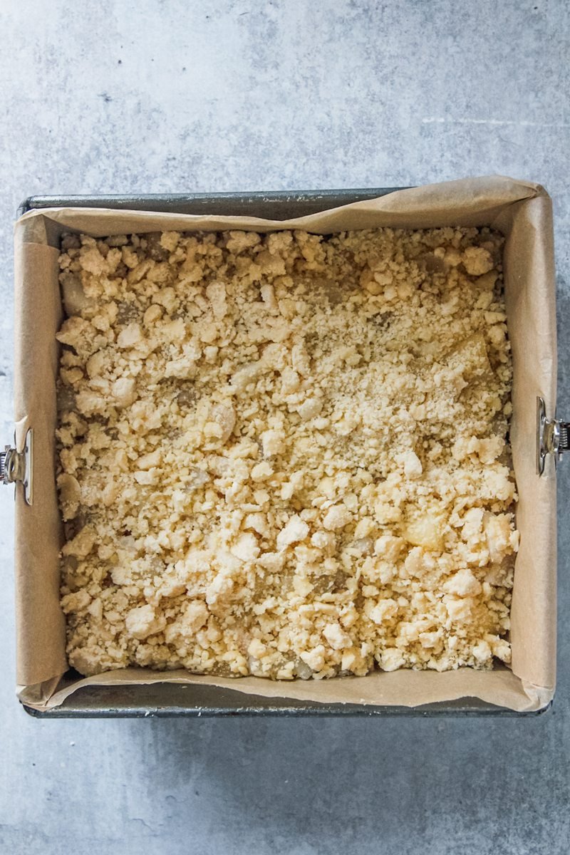 A crumb mixture sits on top of unbaked apple bars on a gray surface.