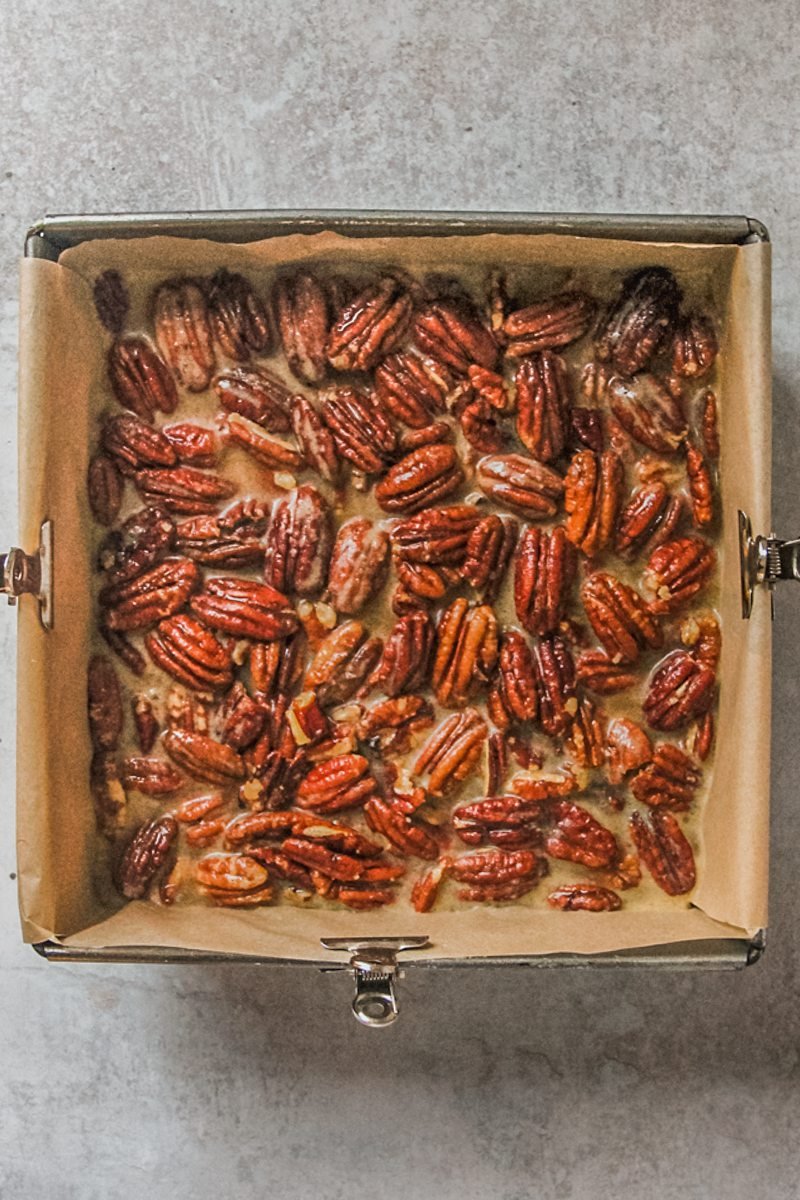 Pecan pie mixture sits in a lined square metal baking tin on a gray surface.