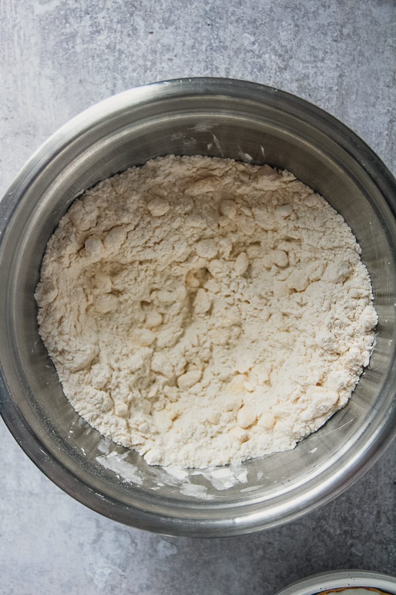 Butter mixed into flour sits in a stainless steel bowl on a gray surface.