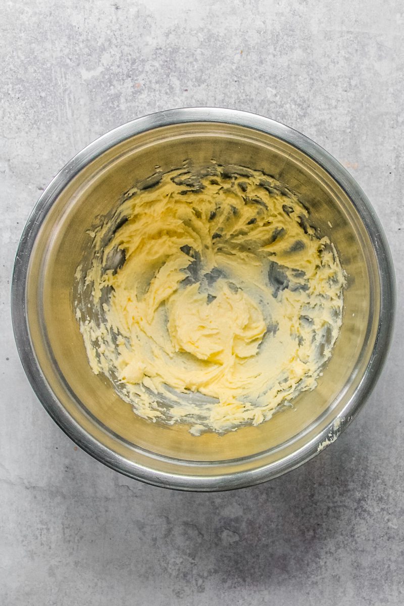 Whipped butter and sugar sits in a stainless steel bowl on a gray surface.