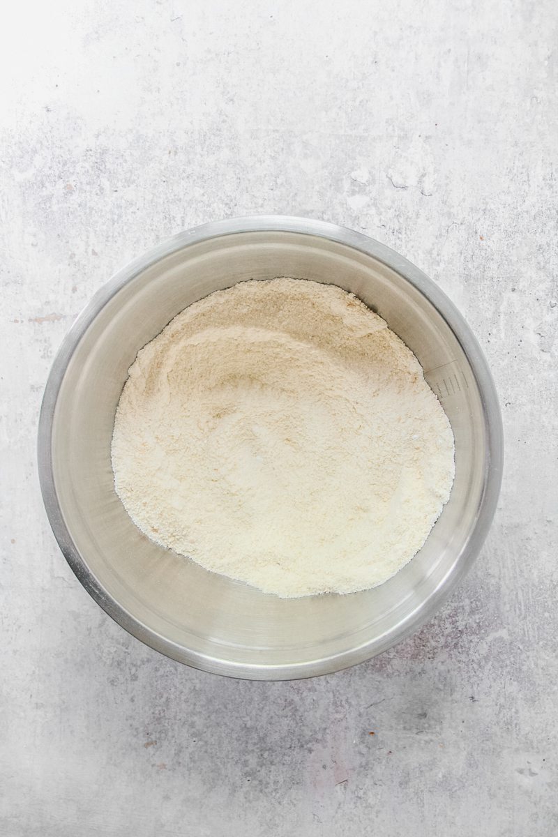 Dry ingredients with butter whipped in, sit in a stainless steel bowl on a gray surface.