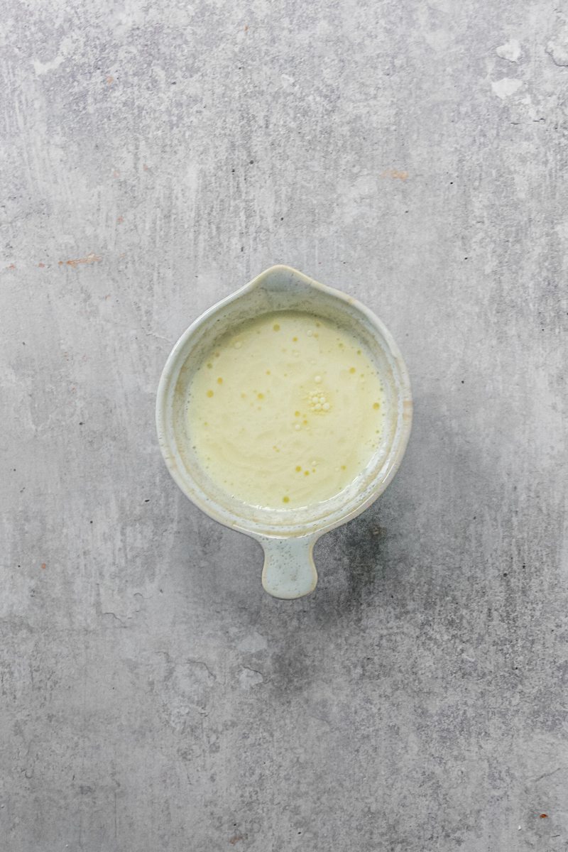 A buttermilk almond extract mixture sits in a small beaker on a gray surface.
