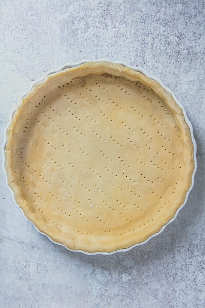 Treacle tart pastry sits pressed into a white ceramic baking dish on a gray surface.