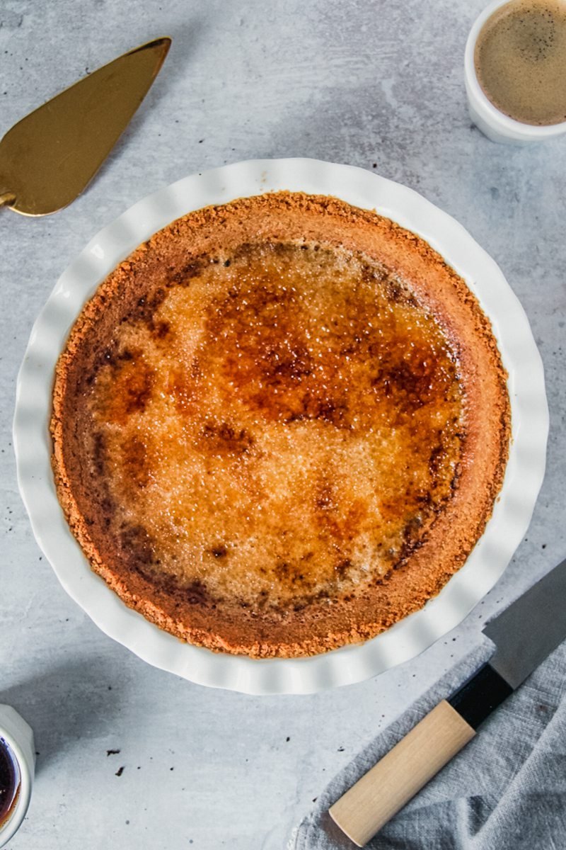 Baked coffee creme brulee sits caramelized in a ceramic white pie dish on a gray surface.