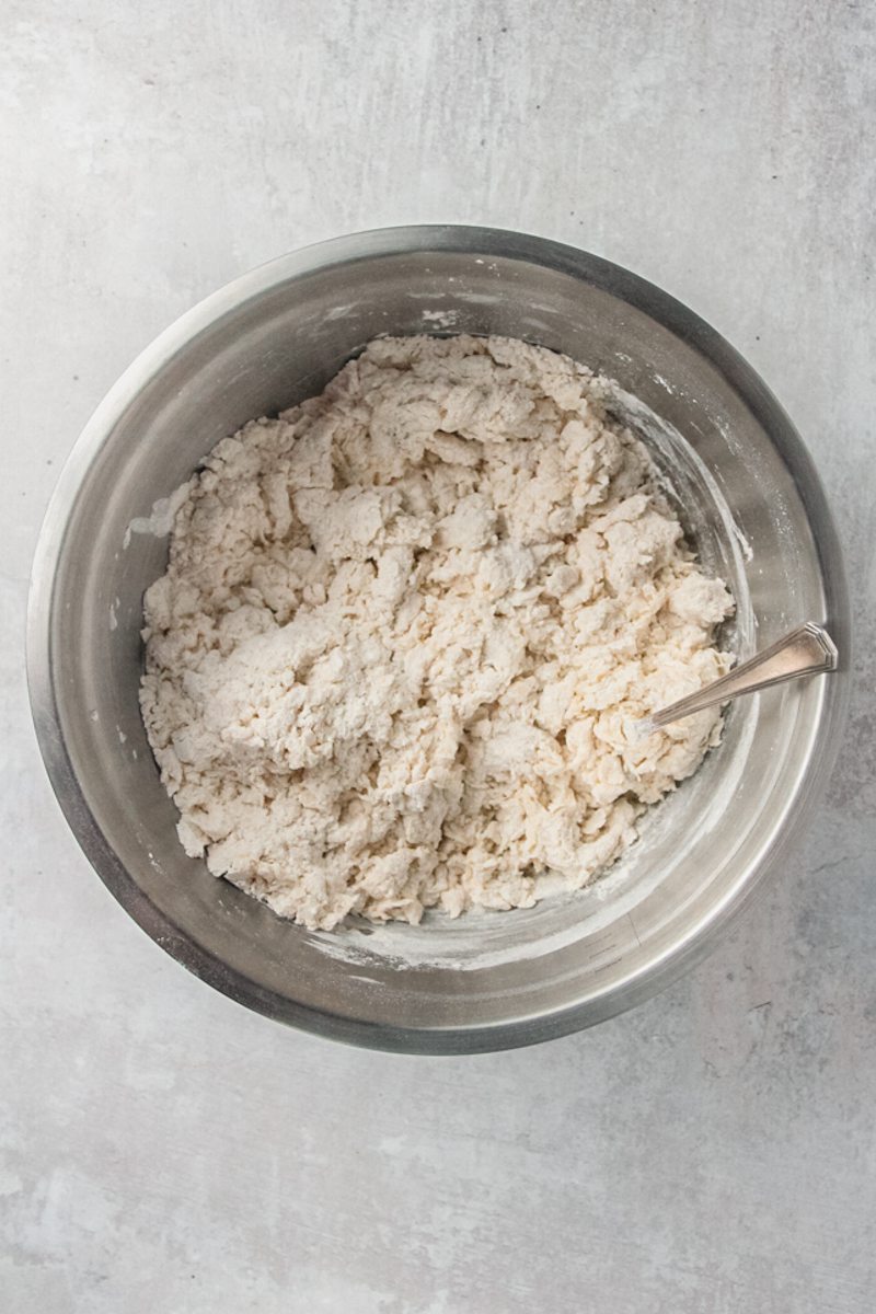 A shaggy dough sits in a stainless steel bowl on a gray surface.