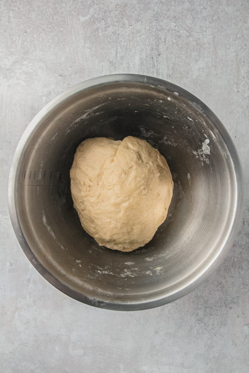 A ball of dough sits in a stainless steel bowl on a gray surface.