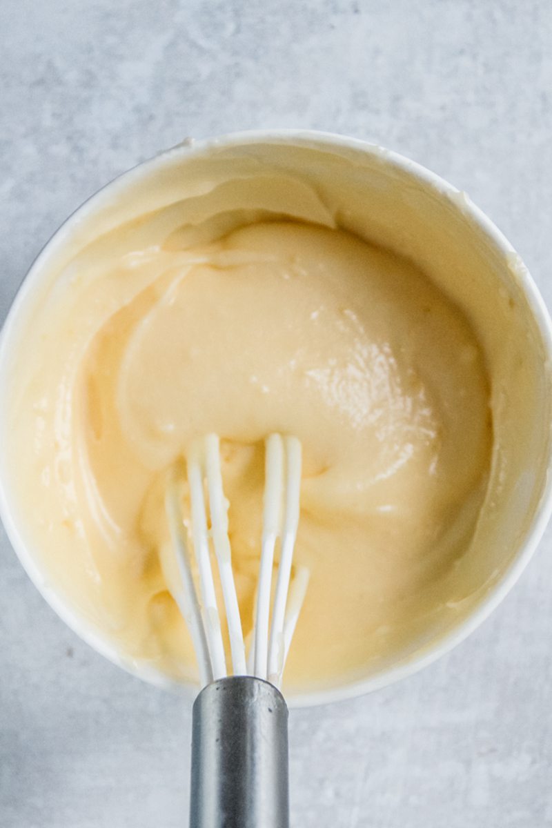 A lemon curd filling for lemon rolls sits in a white ceramic bowl on a gray surface.