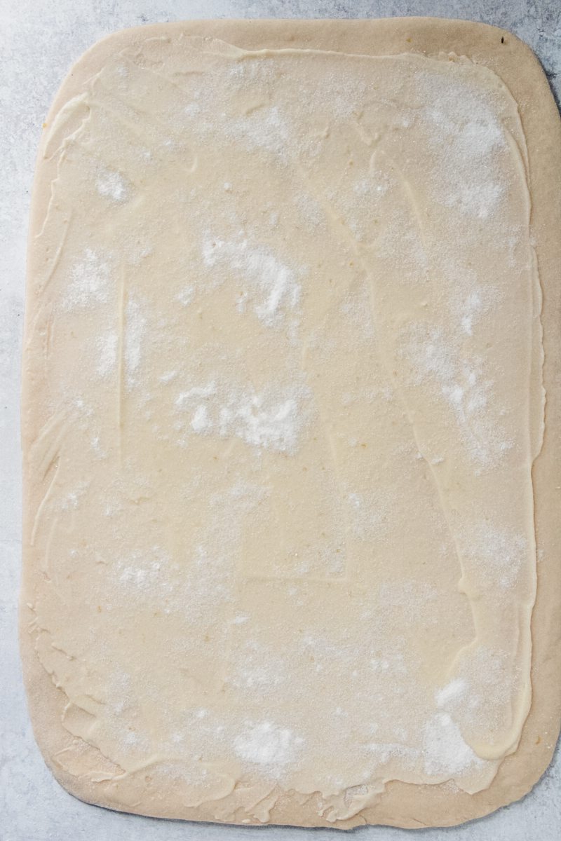 Rolled out dough with a lemon curd topping sits on a gray surface.