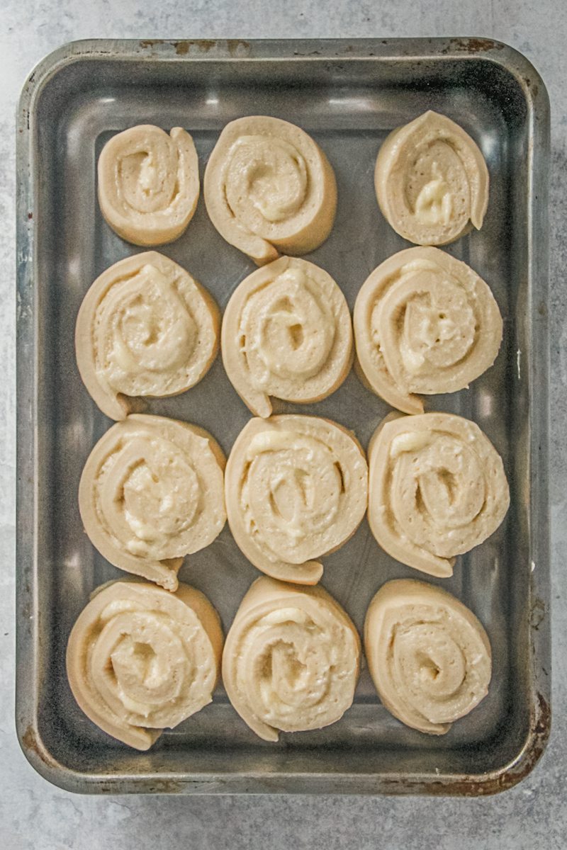 Unbaked lemon rolls sit in a rectangle metal baking tin on a gray surface.