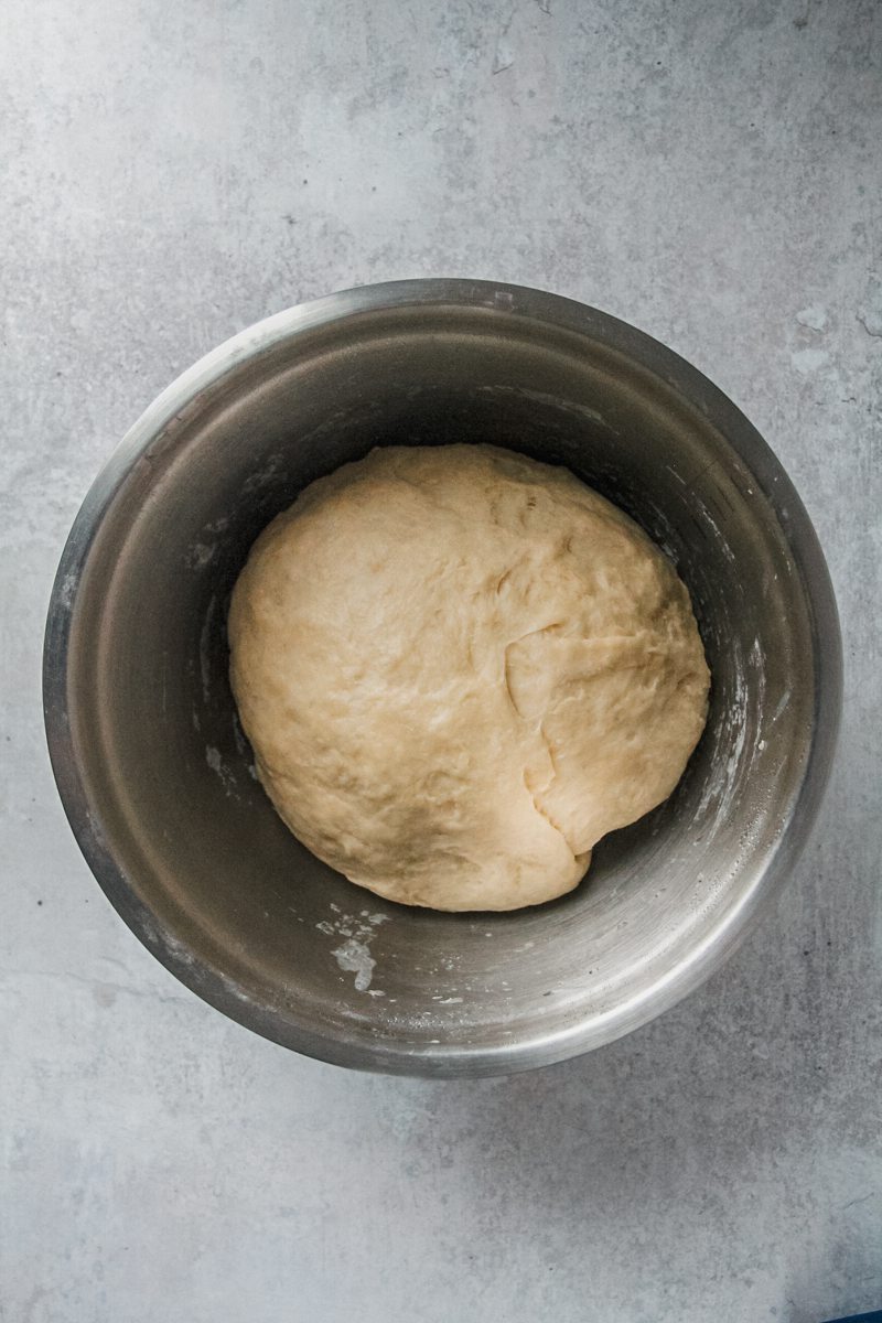 A ball of dough sits in a stainless steel bowl on a gray surface.