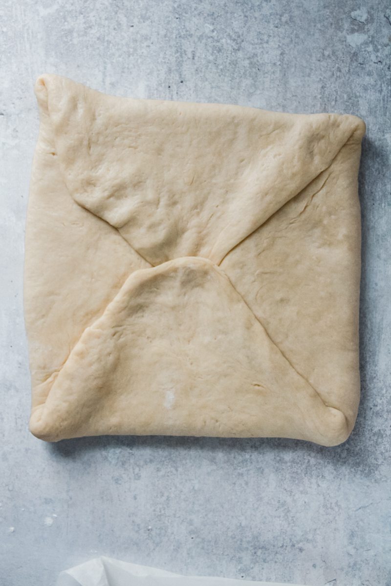 A square of dough sits folded like an envelope over a square of butter on a gray surface.