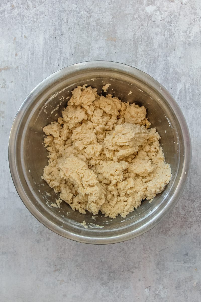 A rough crumble mixture sits in a stainless steel bowl on a gray surface.