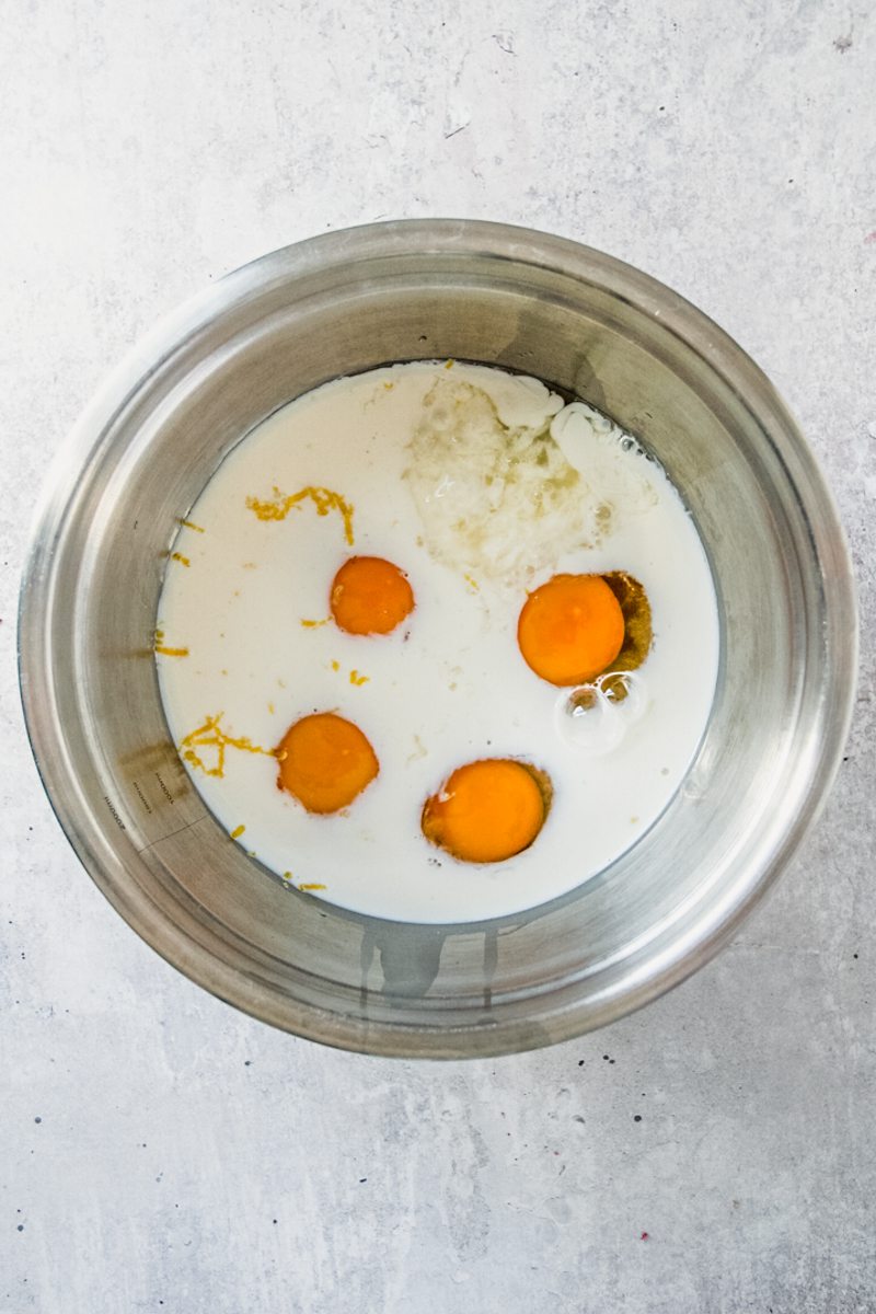 Eggs and milk sit in a stainless steel bowl on a gray surface.