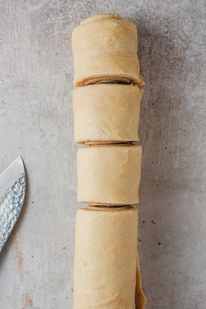 Evenly cut rolls of cinnamon dough sit on a gray surface.