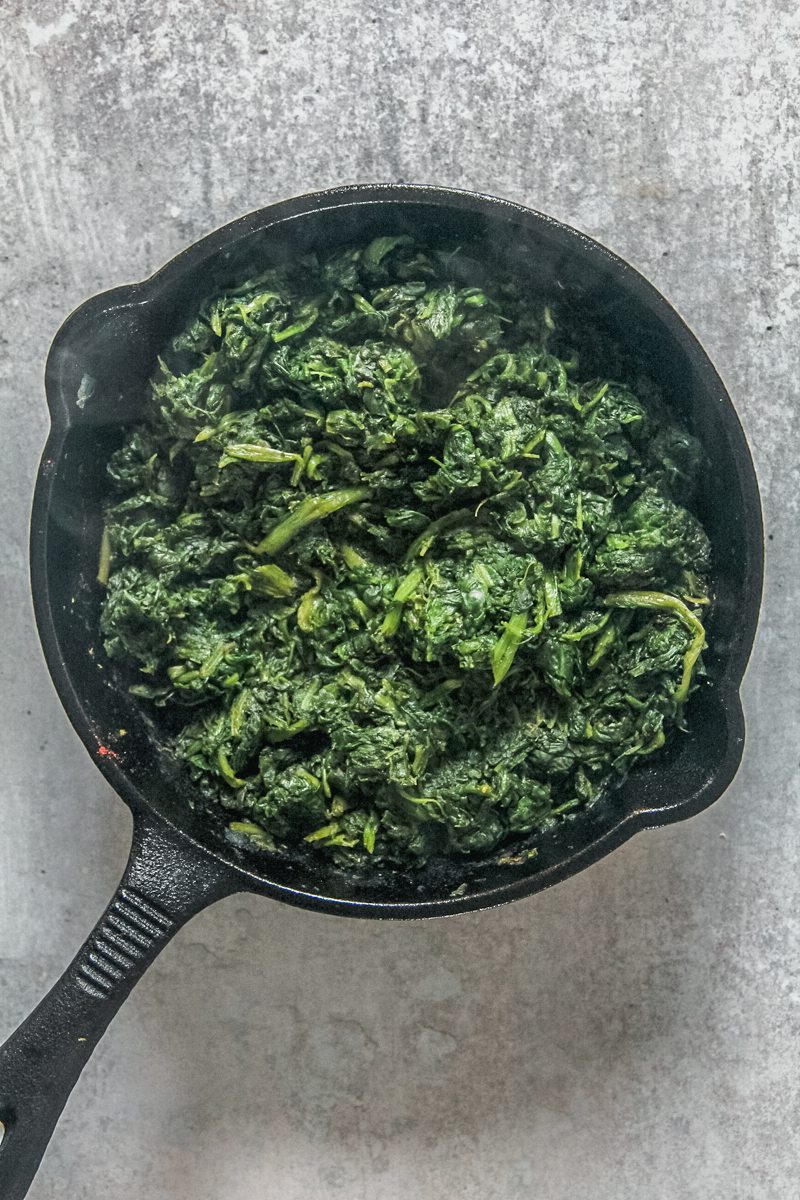 Cooked frozen spinach sits in a cast iron skillet on a gray surface.