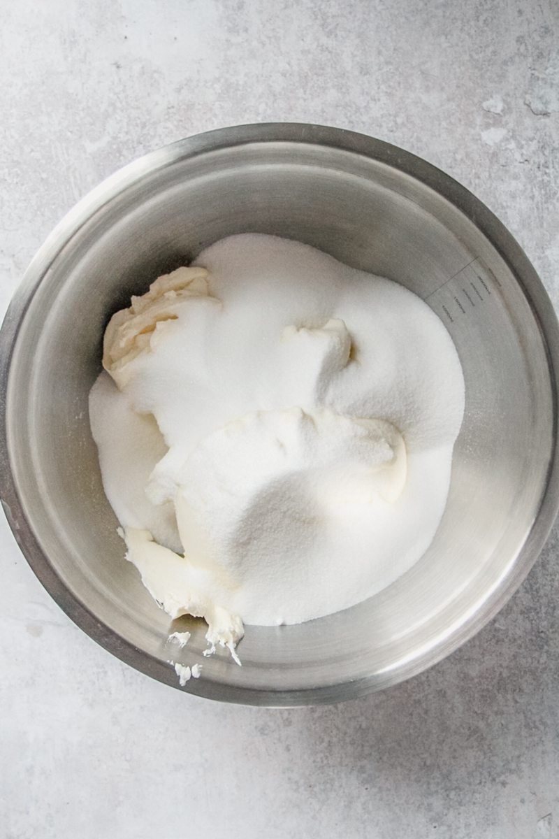 Cream cheese and sugar sit in a stainless steel bowl on a gray surface.