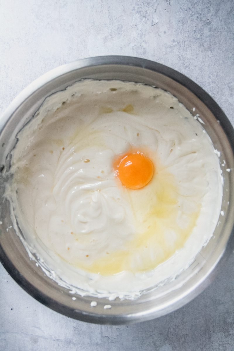 An egg sits in a stainless steel bowl on a gray surface.