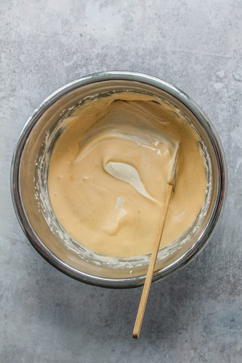 Whipped eggs and whipped cream is stirred into a stainless steel bowl on a gray surface.